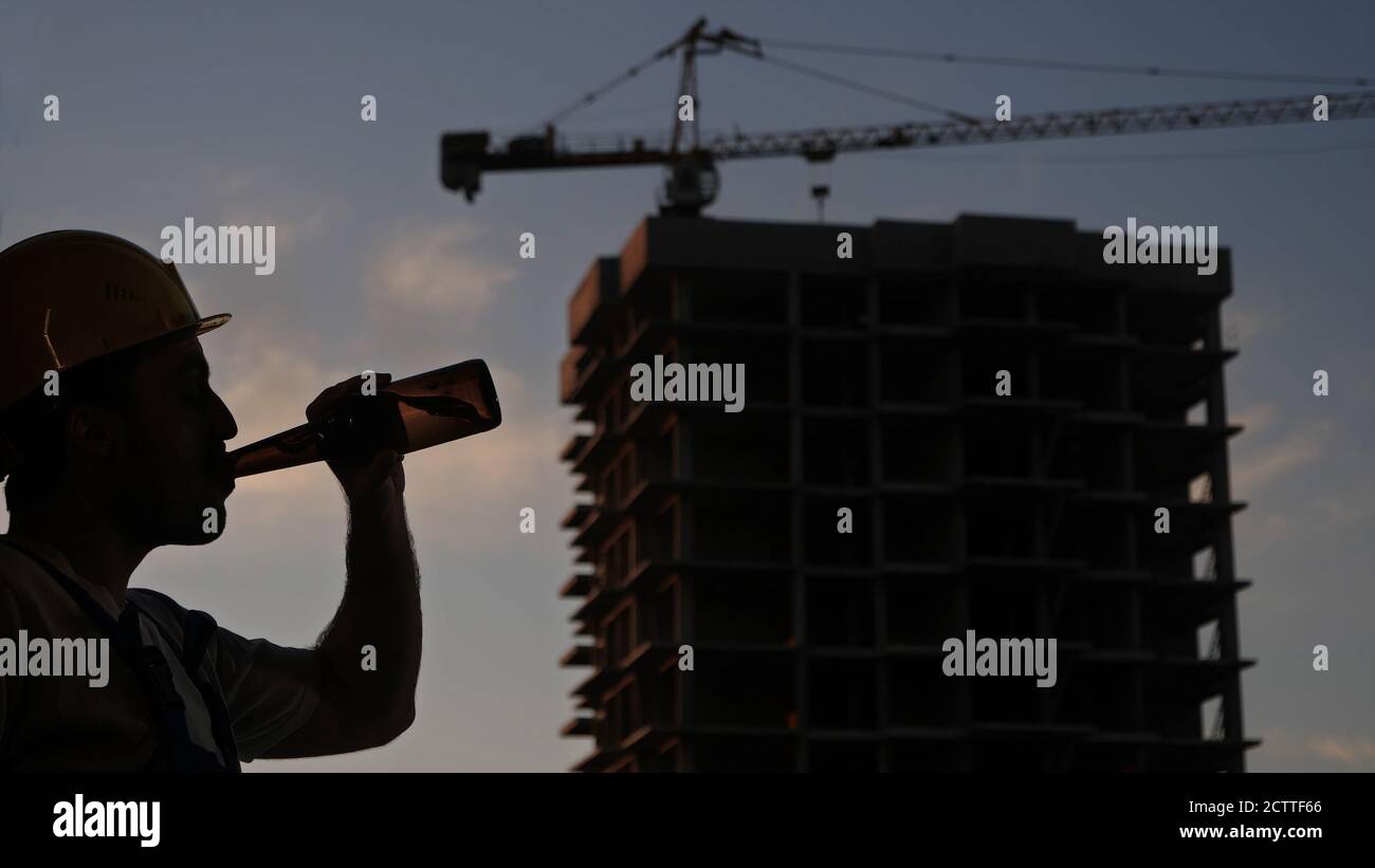 Drunk worker in yellow helmet at construction site. Stock Photo
