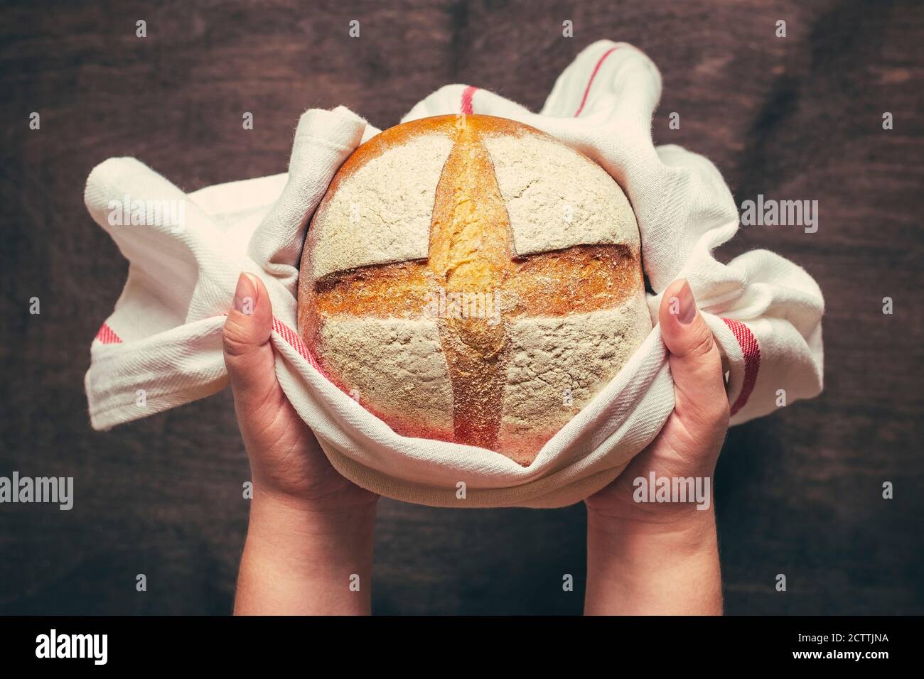 female hands holds freshly baked sourdough bread in napkin from oven on blue wooden table Top view Flat lay Homemade pastry Stock Photo