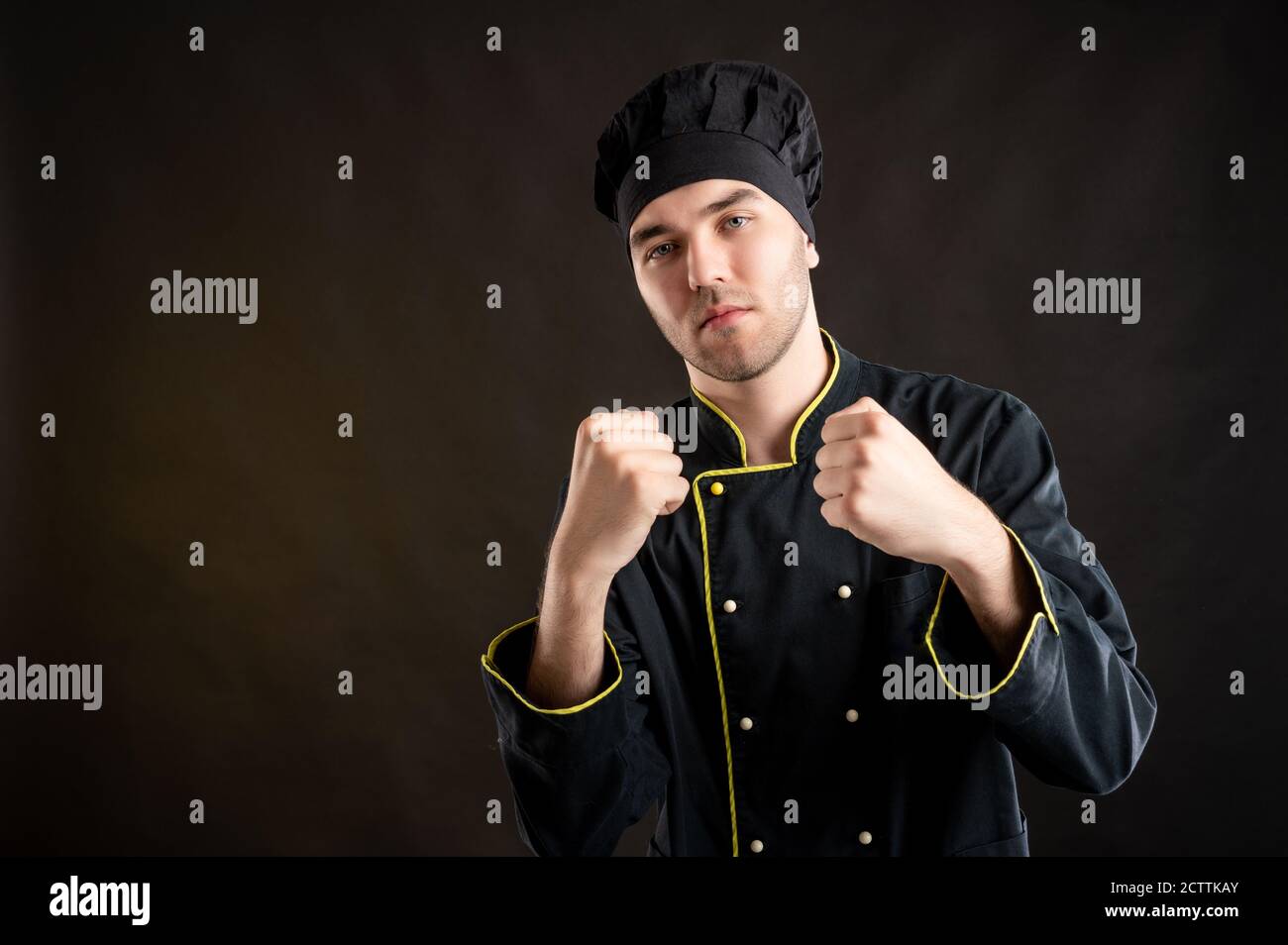 Portrait of young male dressed in a black chef suit showing fists ...