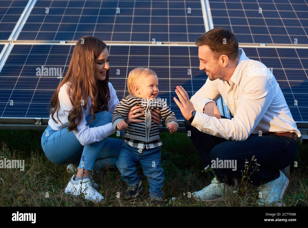 Dad, mom and baby on the background of solar panels on a warm day. The concept of family warmth and comfort in the modern world with continuously advancing technology Stock Photo