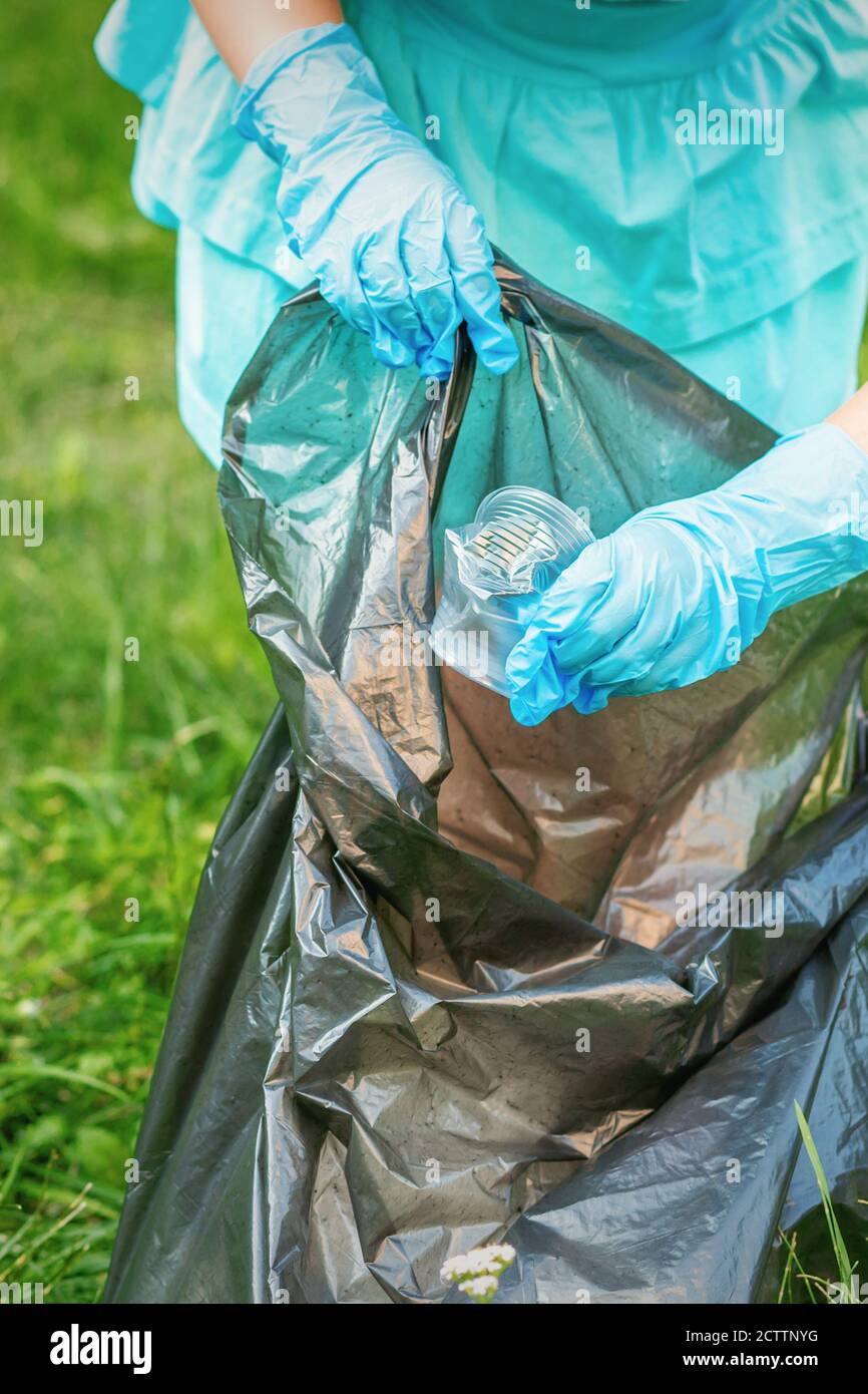 Child collects plastic trash from grass throwing garbage in garbage bag