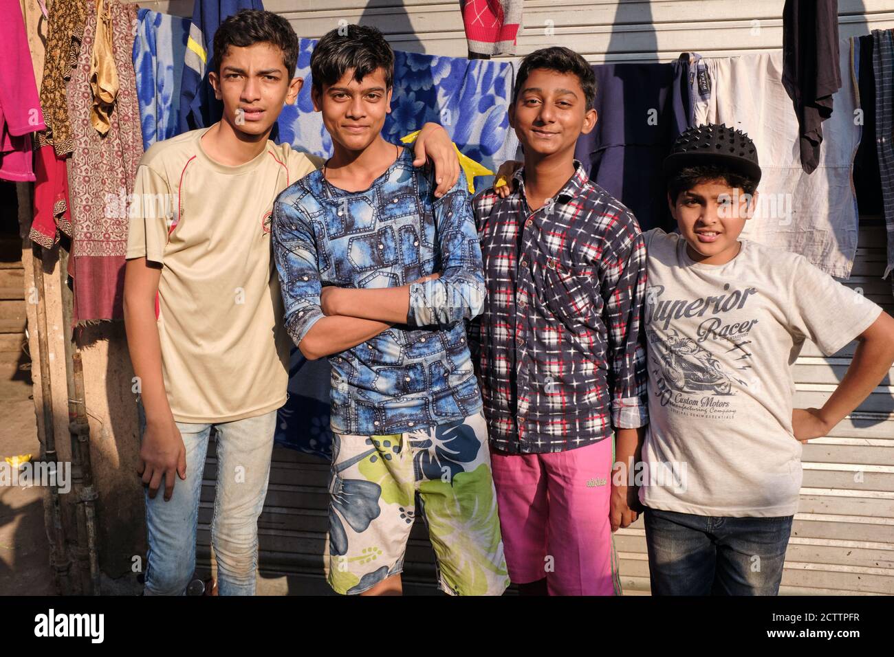 A group of four Indian, mostly teenage boys posing in front of a laundry's washing line in Chor Bazar area, Bhendi Bazar, Mumbai, India Stock Photo