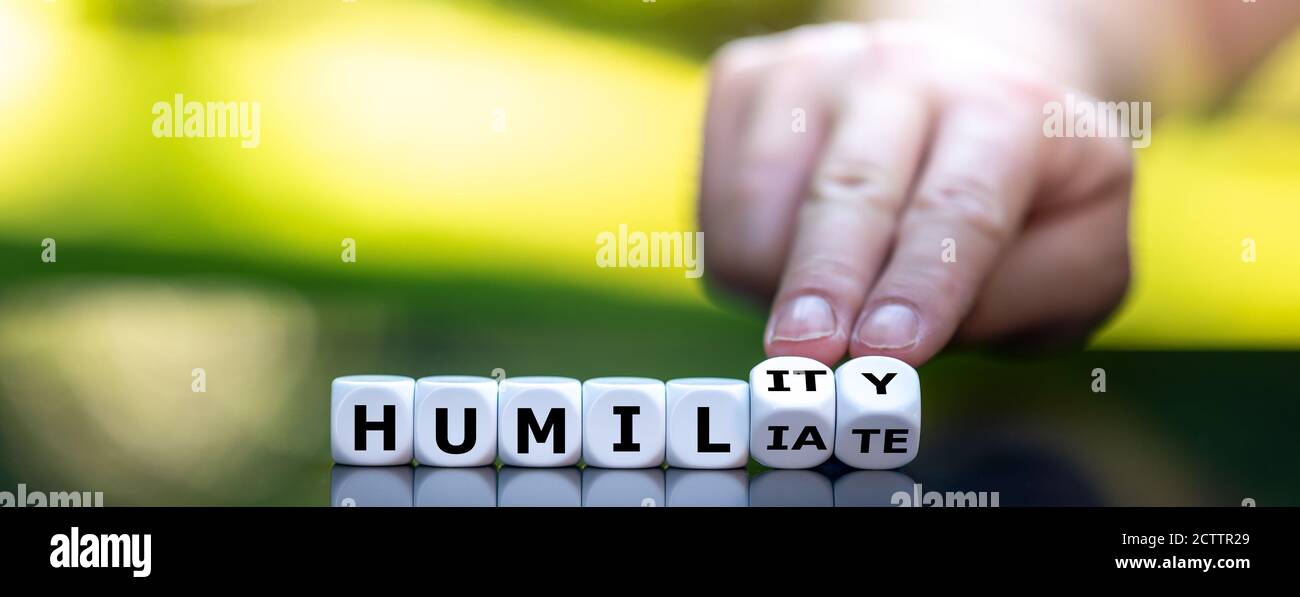 Hand turns dice and changes the word 'humiliate' to 'humility'. Stock Photo