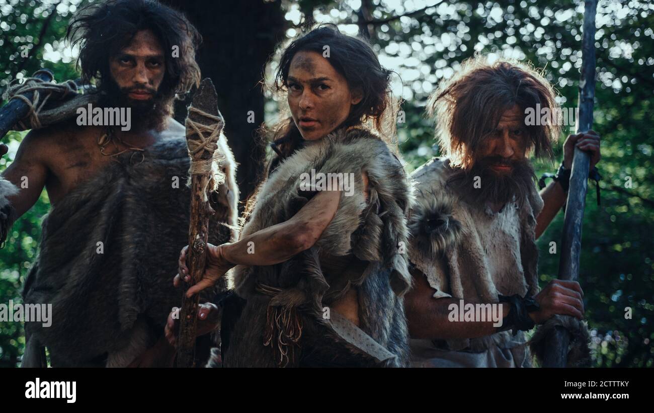Female Leader and Two Primeval Cavemen Warriors Threat Enemy with Stone Tipped Spear, Scream, Defending Their Cave and Territory in the Prehistoric Stock Photo
