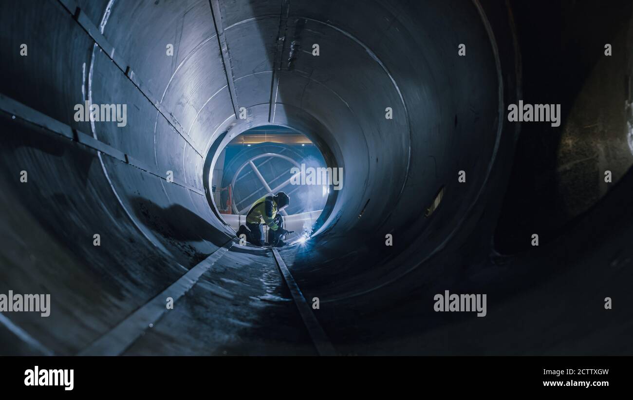 Professional Heavy Industry Worker Wearing Helmet Welding Inside Oil and Gas Pipe. Construction of the Oil, Natural Gas and fuels Transport Pipeline Stock Photo