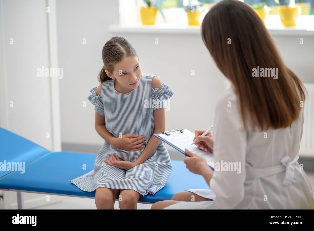 Girl having a stomach ache and talking to the female doctor Stock Photo