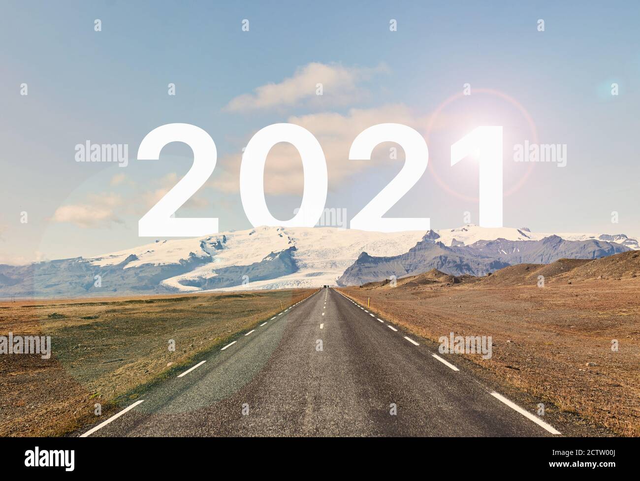 The word 2021 is written behind a glacier and an empty asphalt road against a golden sunset and beautiful blue sky.  Stock Photo
