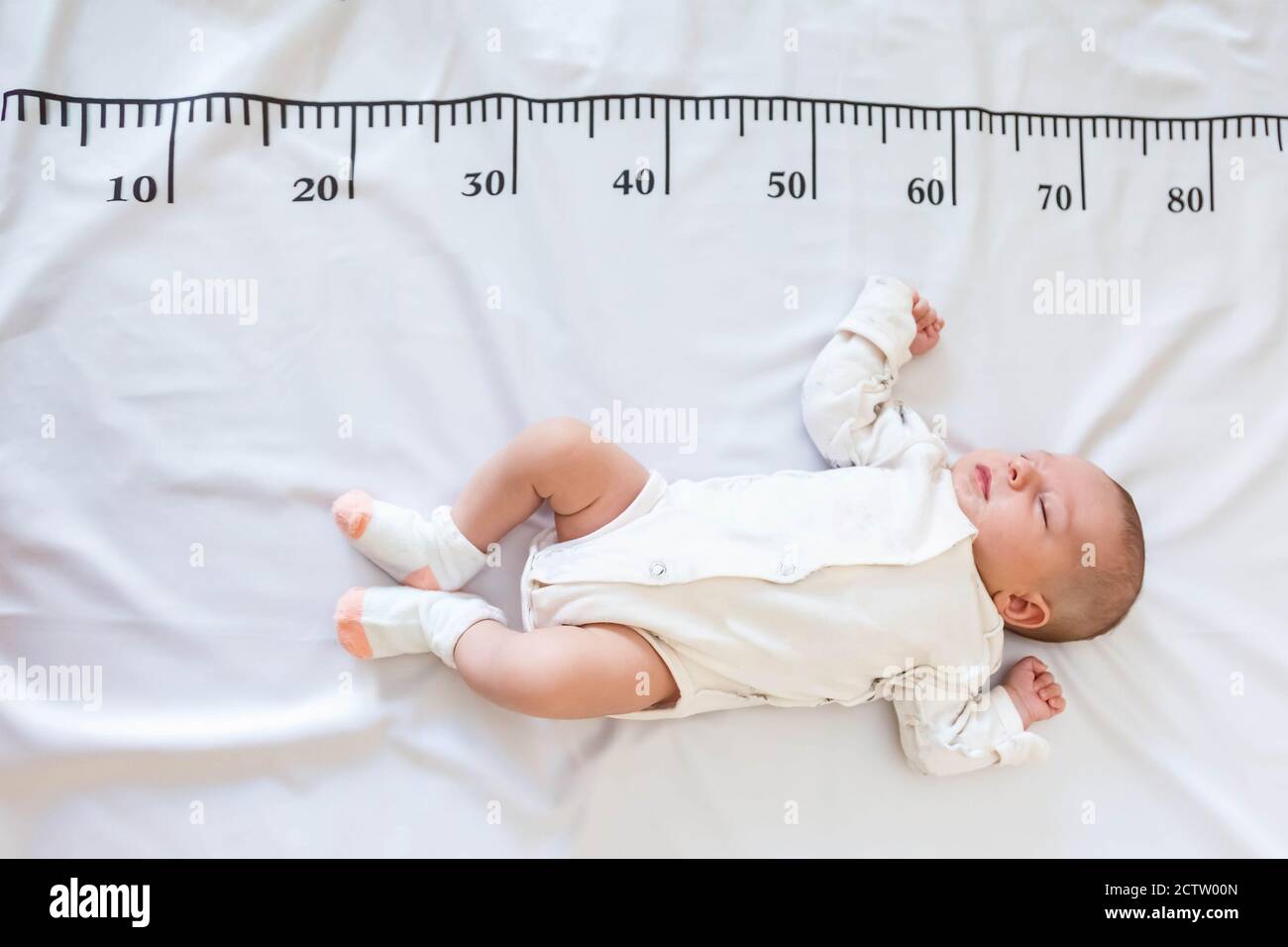 A newborn 2 month baby in white sleeps on a bed on which a measuring