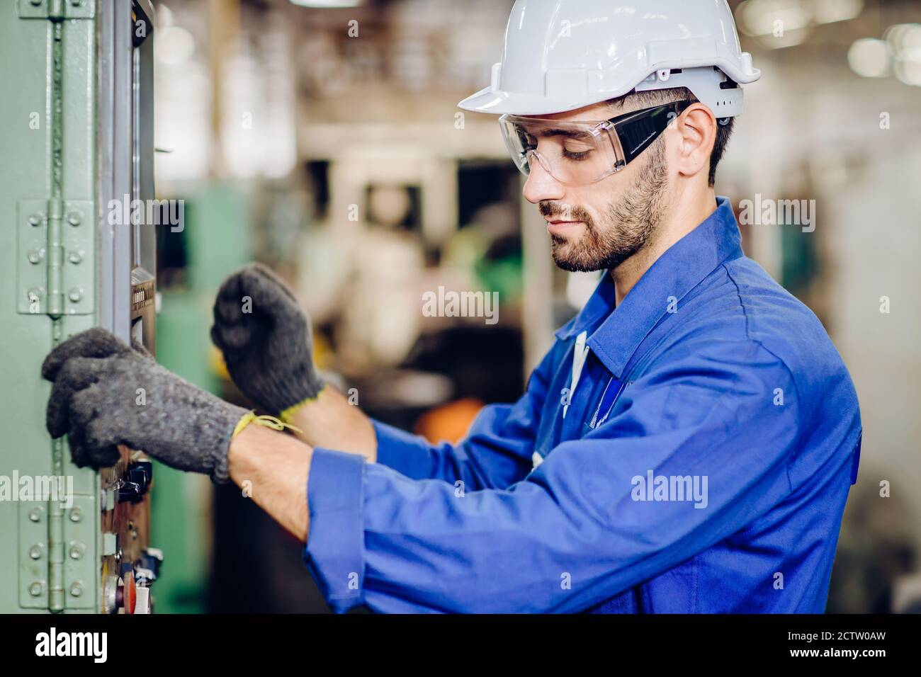 Hispanic latin labor worker hard working with safety glasses and helmet with heavy metal machine in factory industry . Stock Photo