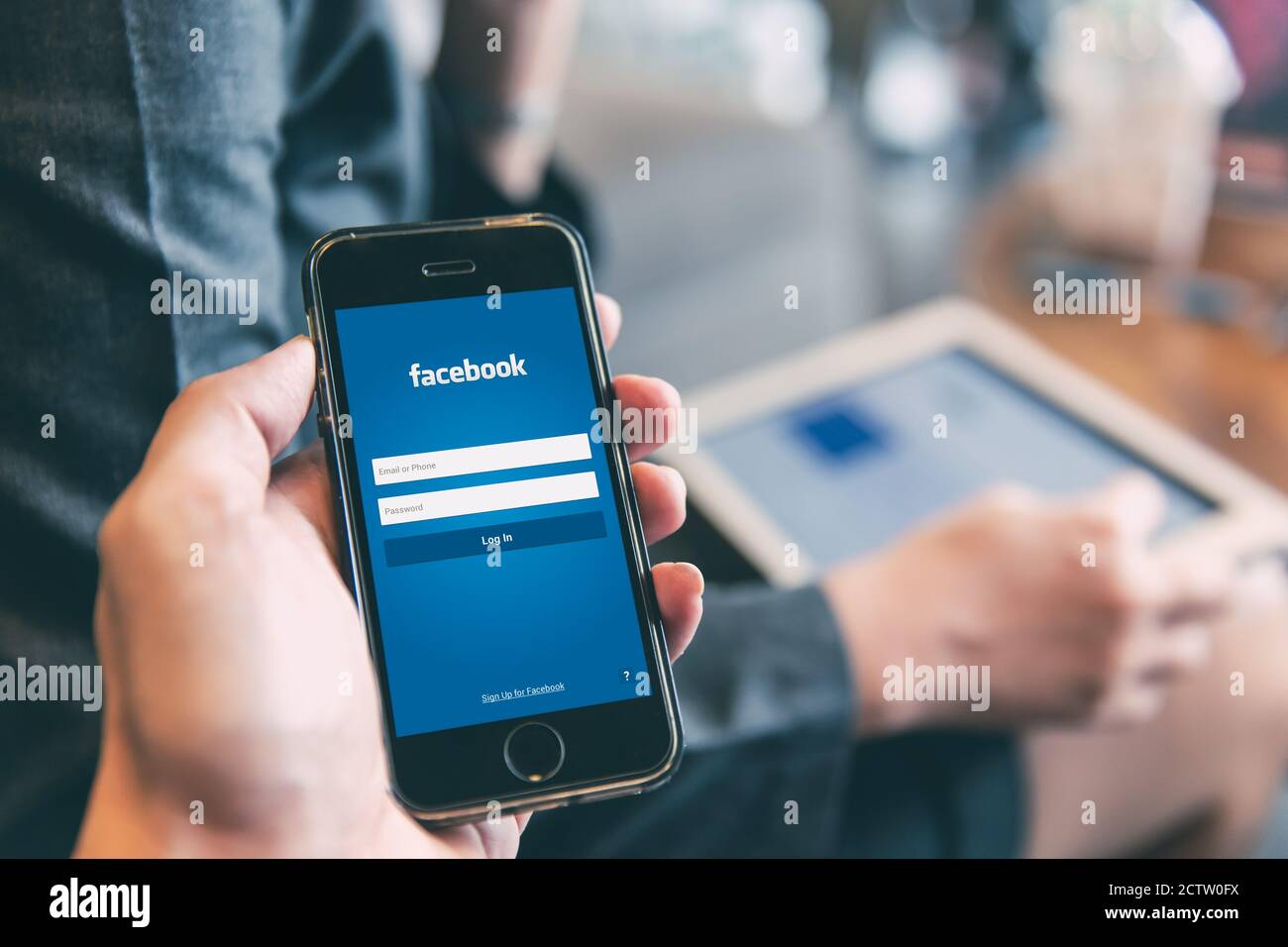Facebook App login page on iPhone with people using tablet background for social network security on mobile smartphone.,20 July 2019,Bangkok, THAILAND Stock Photo