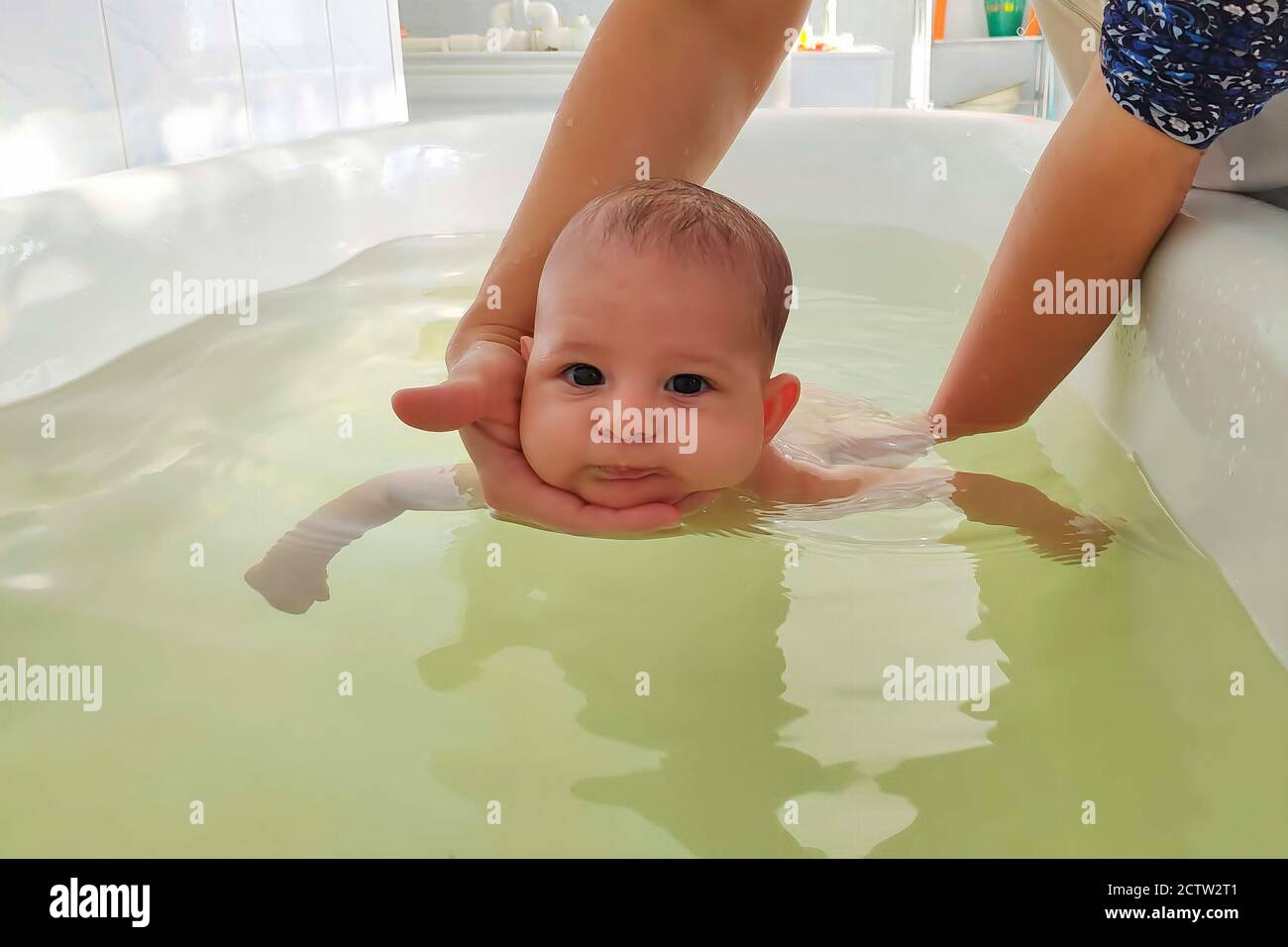 Infant baby in special pool with doctor instructor. Newborn children swimming, teaching. Hands holding child in bath Stock Photo