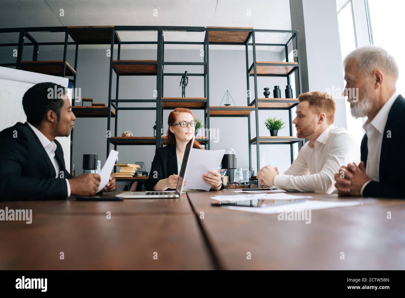 Motivated business woman leader holds meeting with employees at office desk, shooting from below. Stock Photo