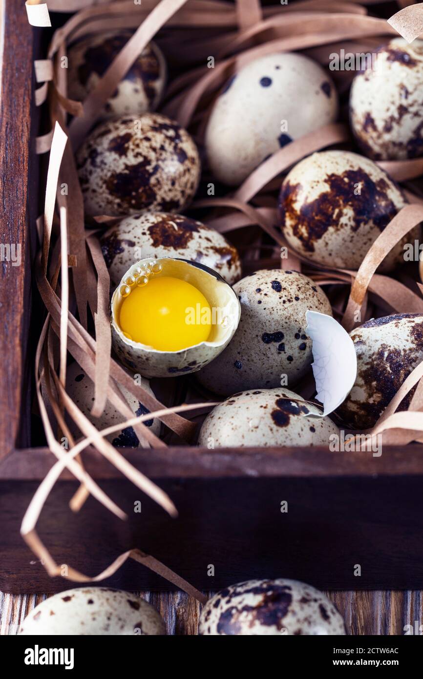 Quail eggs. Flat lay composition with small quail eggs in the wooden box on the natural wooden background. One broken egg with a bright yolk. Quail eg Stock Photo