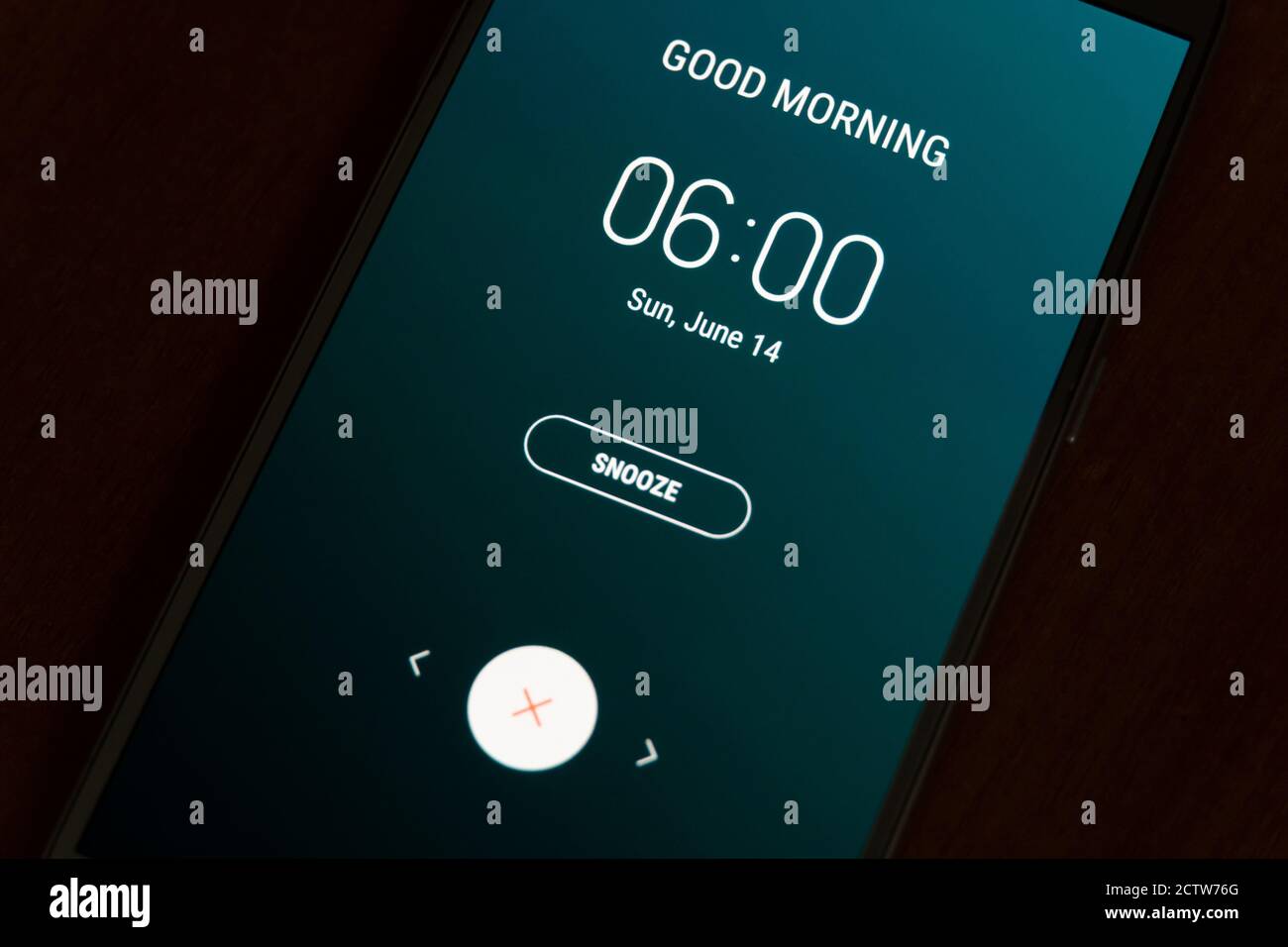 On a black smartphone, an alarm clock rings for 6 am with the inscription Good morning close-up, background Stock Photo