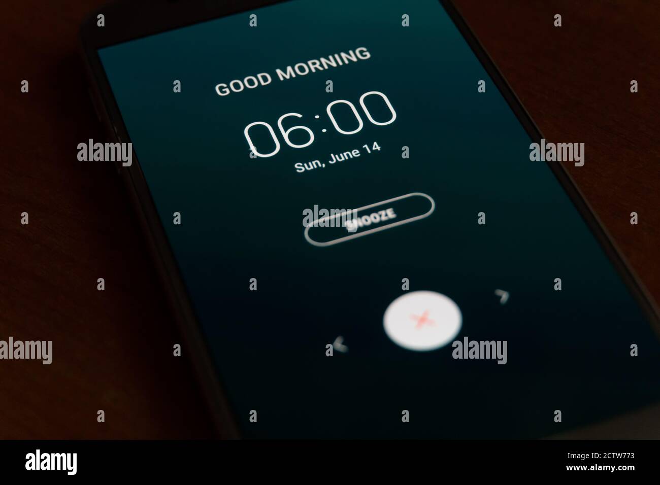 On a black smartphone, an alarm clock rings for 6 am with the inscription Good morning close-up, background Stock Photo