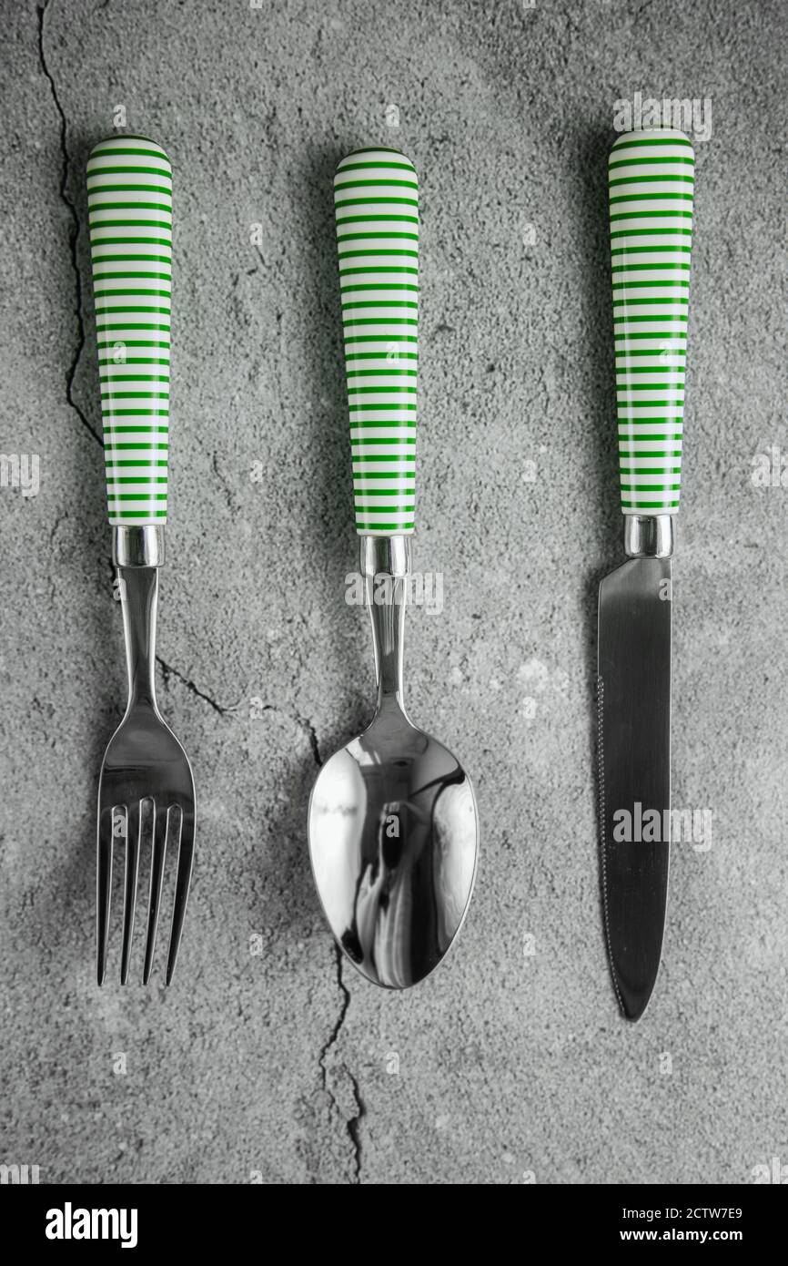 Cutlery on gray concrete background. Spoon, fork, knife with white and green stripes on handles Stock Photo