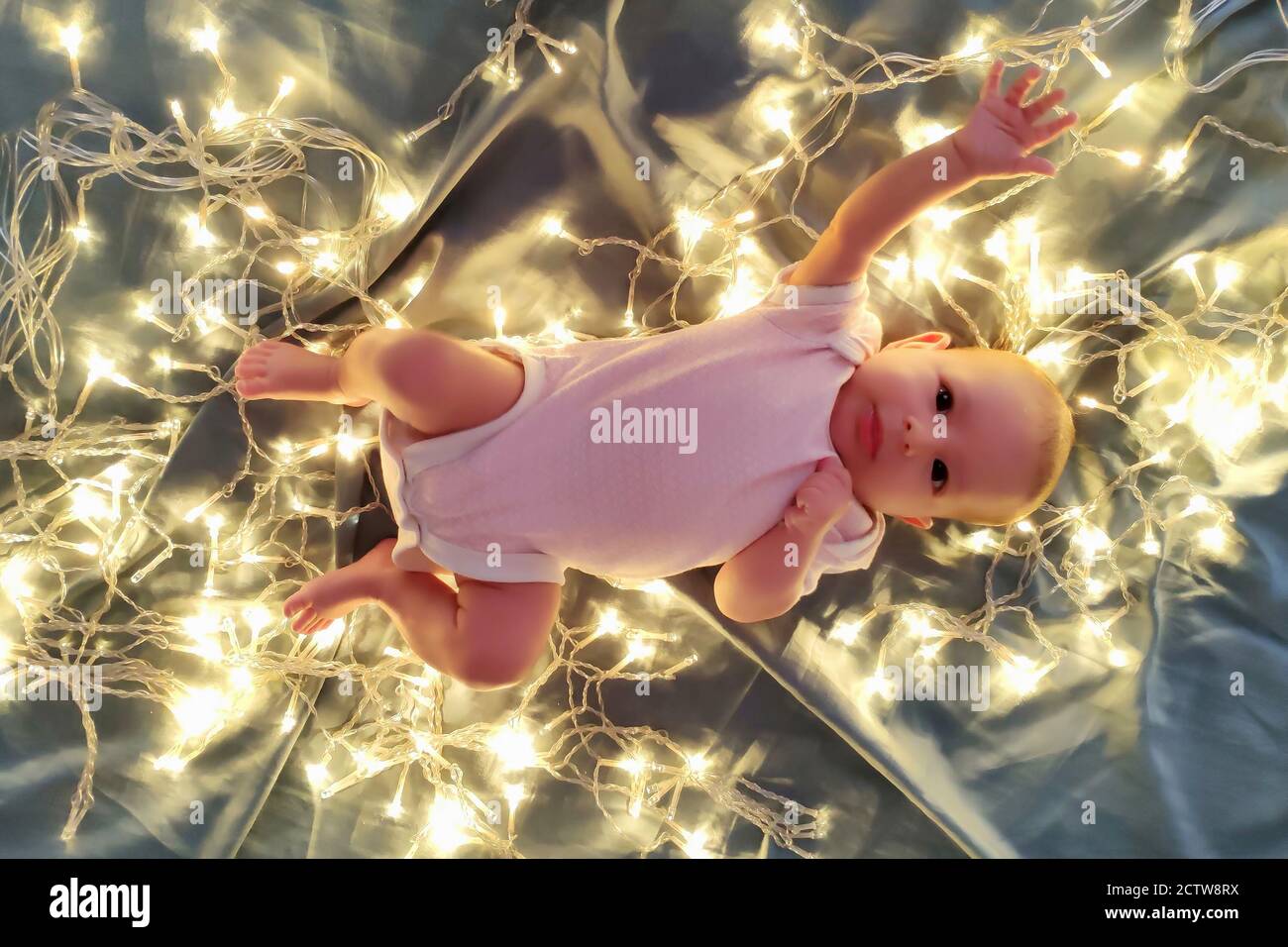 A newborn baby is lying on the bed with Christmas lights and stretching
