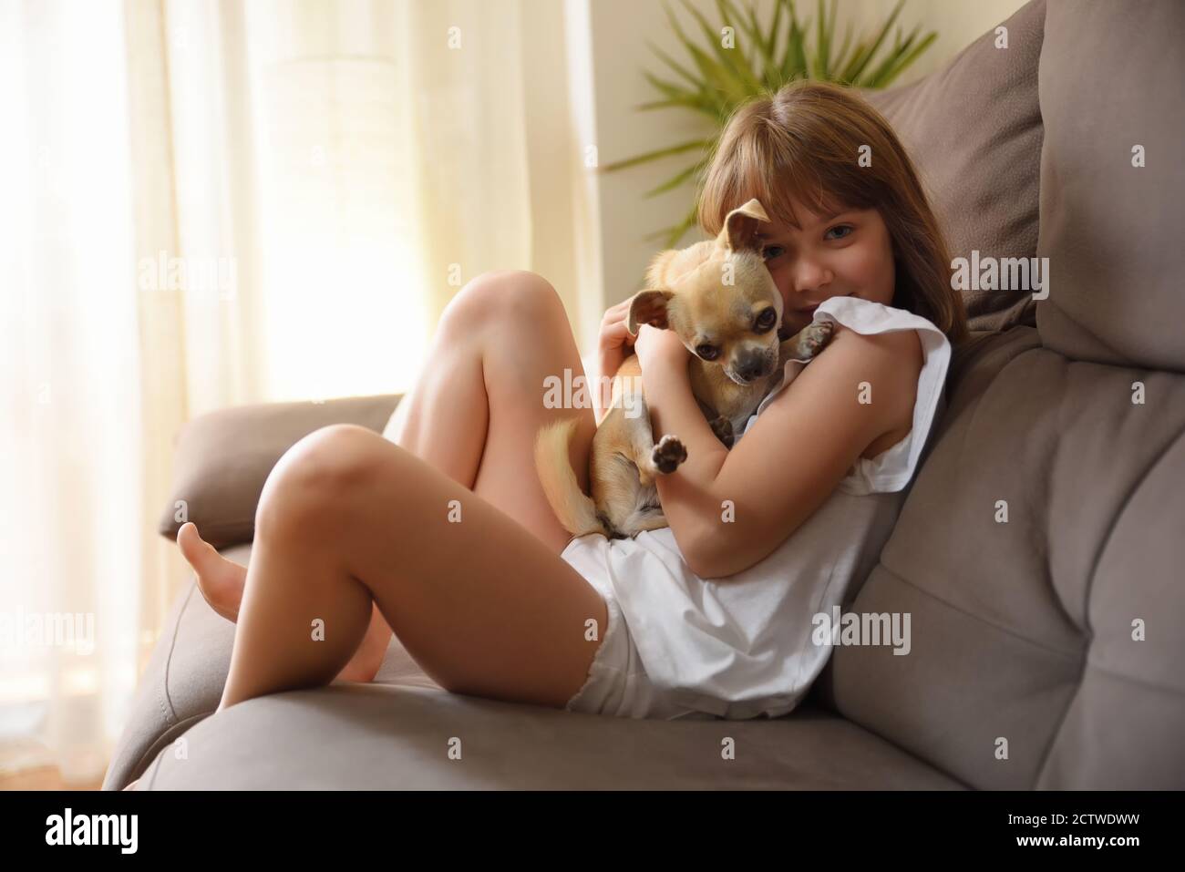 Laughing girl holding her dog affectionately on the sofa looking at camera Stock Photo