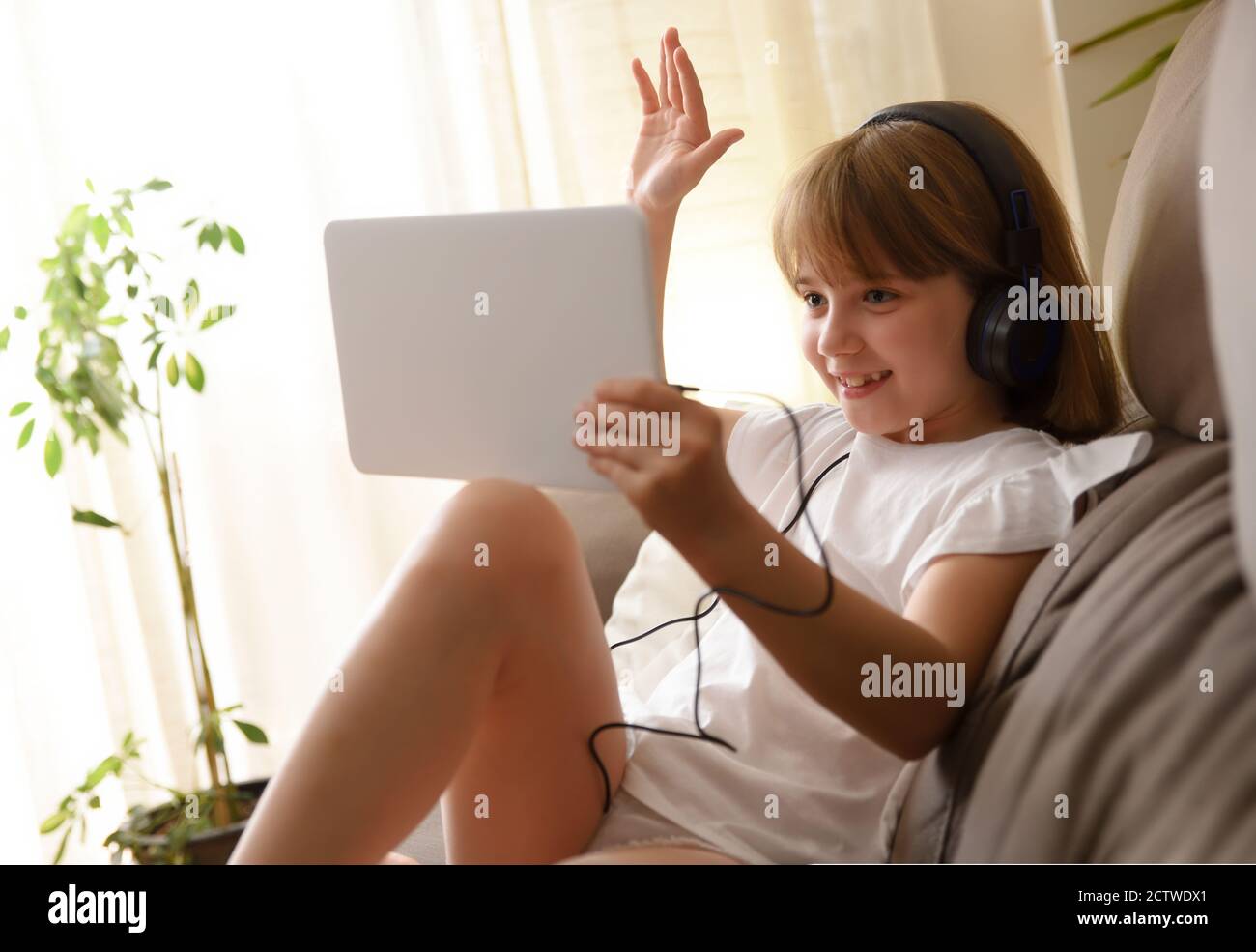 Happy little girl sitting on the sofa in her living room waving by ...