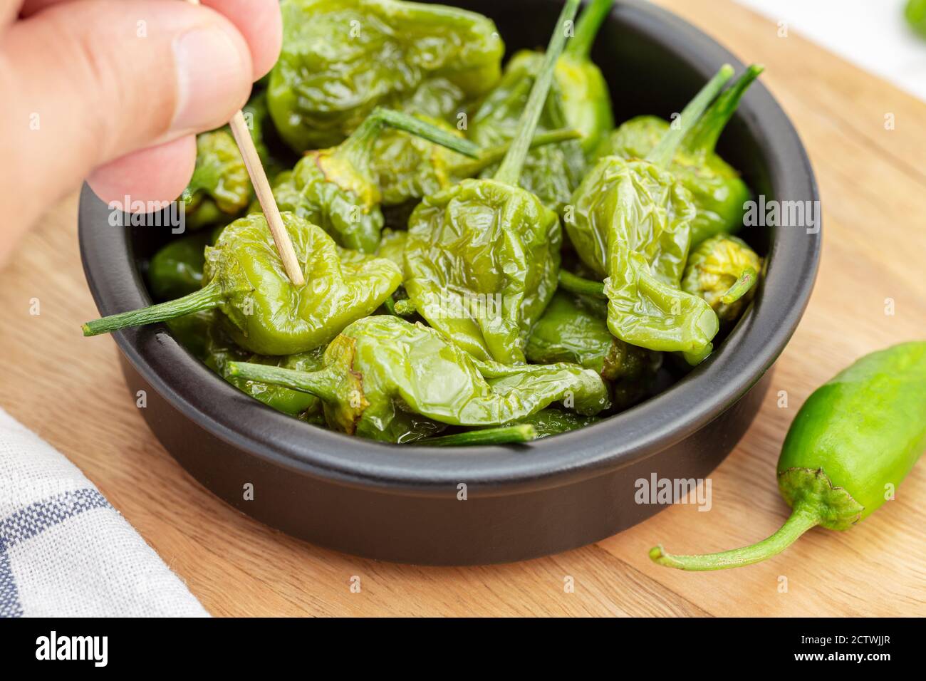 Hand picking a Cooked Padron peppers in a a bowl. Traditional Spanish appetizer Stock Photo