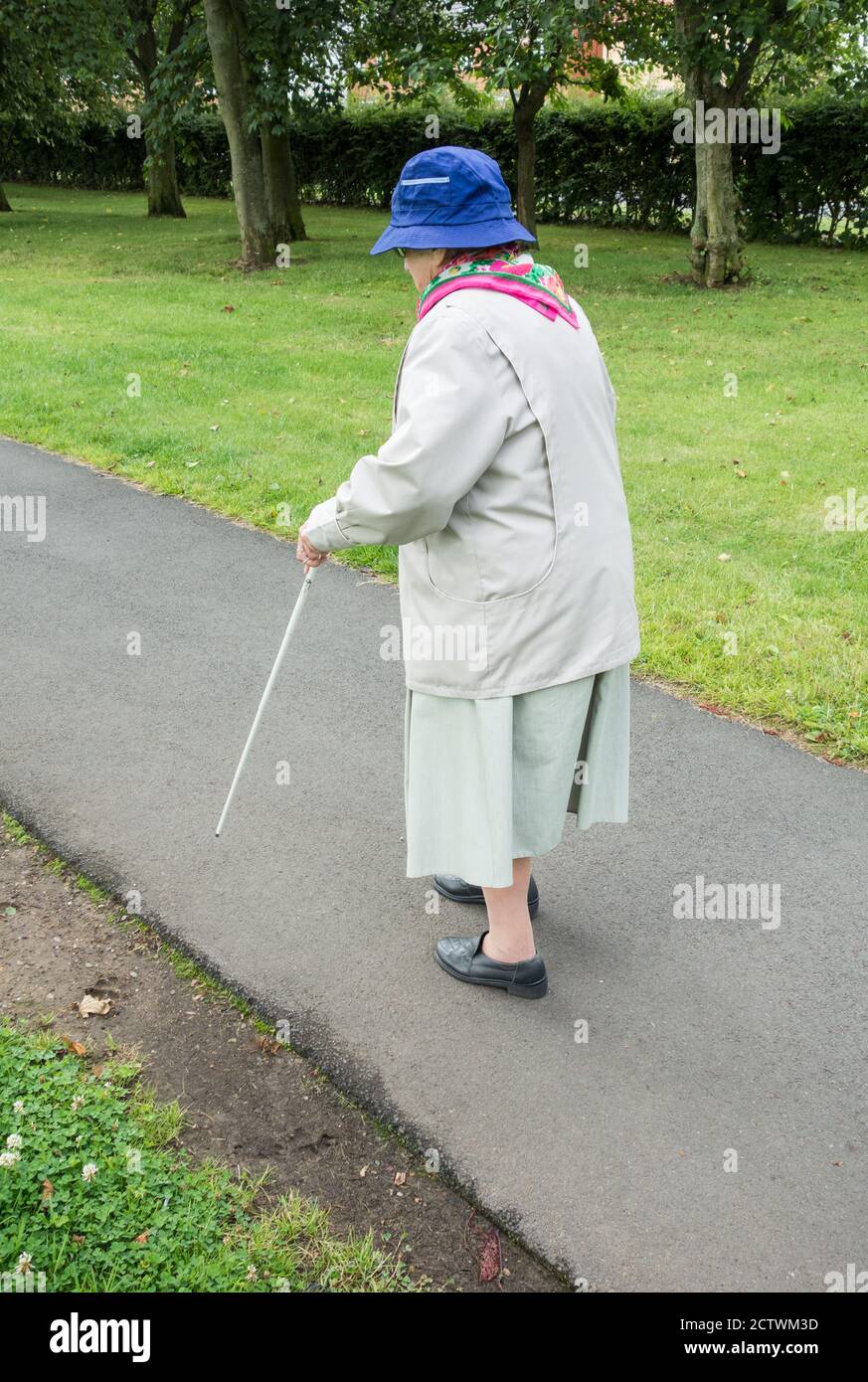 Ninety year old visually impaired lady with white stick sitting on bench in public park. England, UK Stock Photo