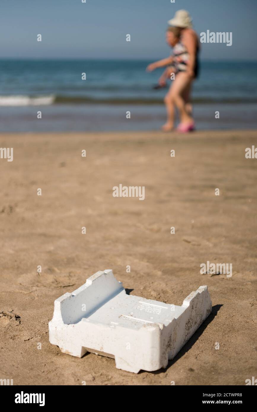 Plastic, white, styrofoam container left on sandy beach with walking people. Stock Photo