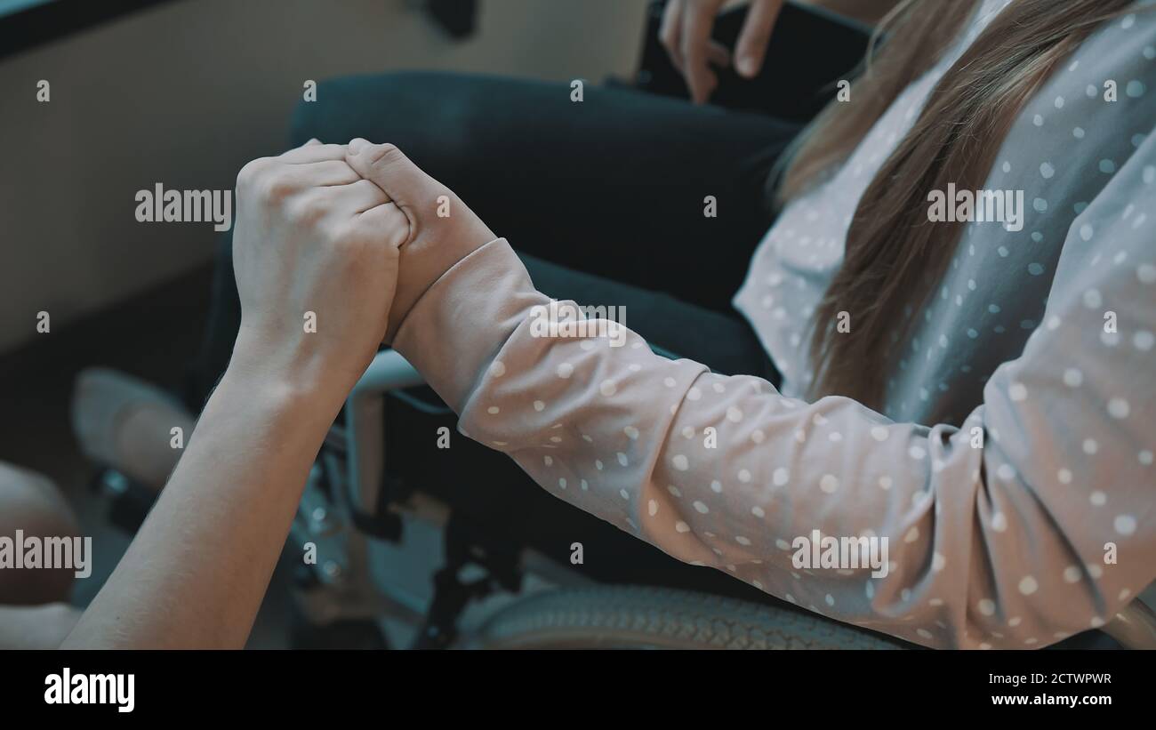Close up, hand holding the hand of young woman recovering in the wheelchair. High quality photo Stock Photo