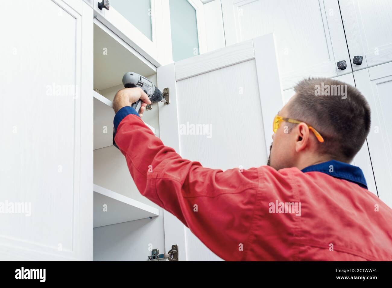 Worker using cordless screwdriver while installing new furniture in kitchen Stock Photo