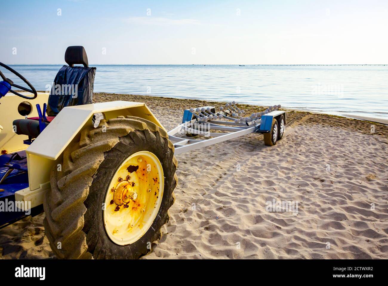 Tractor with empty trailer is parked on the sandy beach, waiting for transport boats. Stock Photo