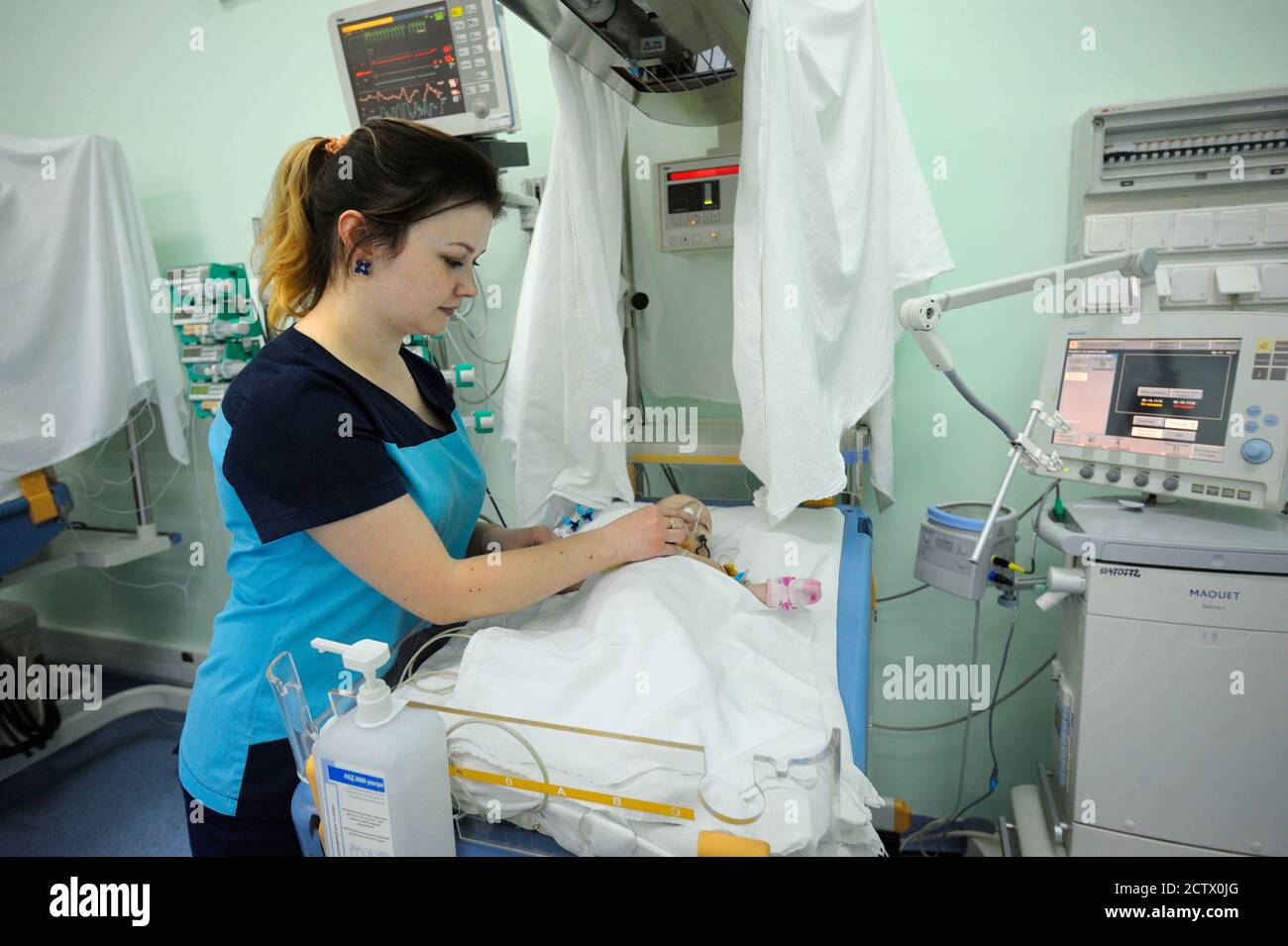 At the intensive care unit. Nurse standing near hospital bed with a baby attaching it to the reviving apparatus. Ukrainian Children's Cardiac Center. Stock Photo