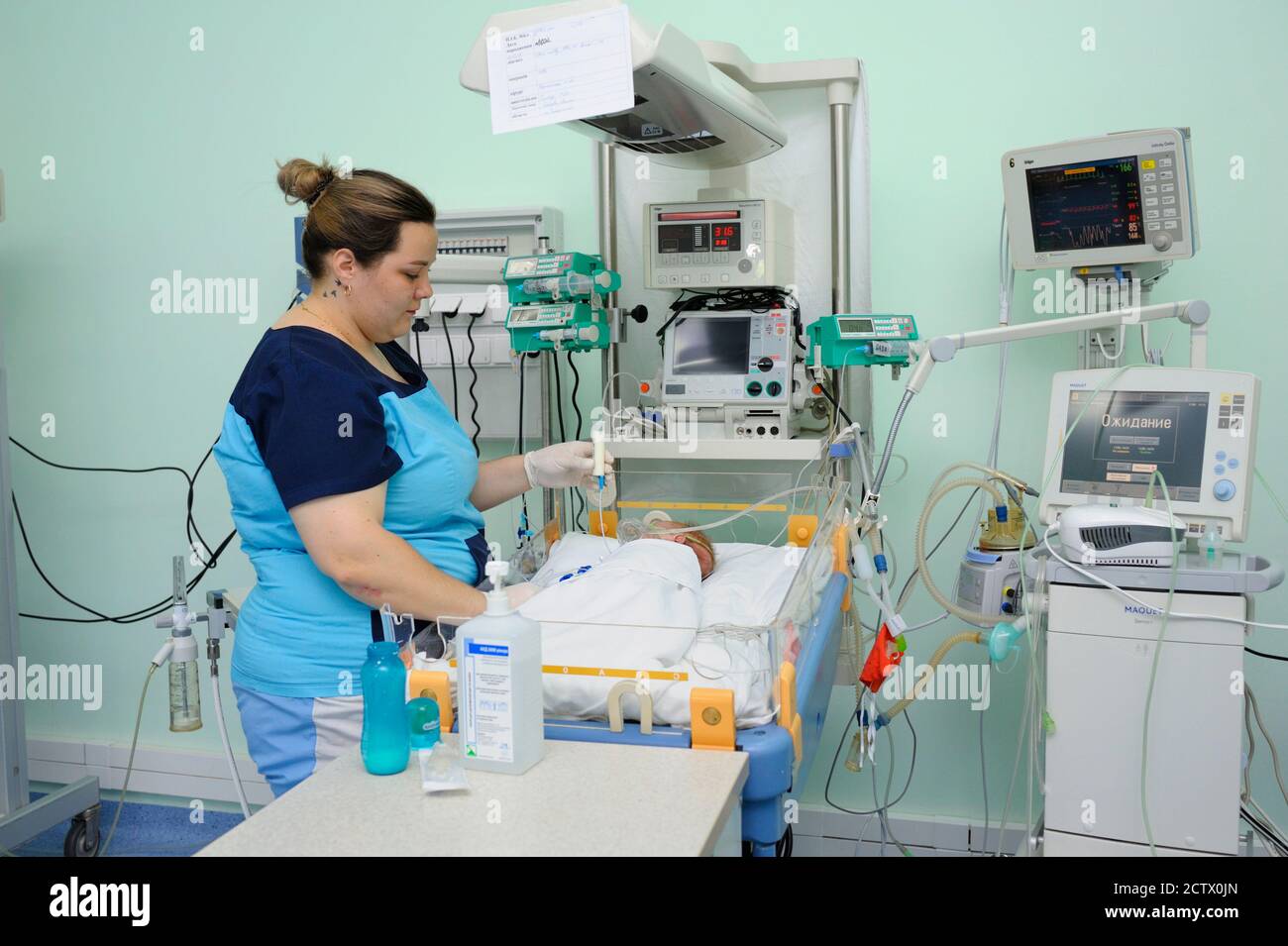 At the intensive care unit. Nurse standing near hospital bed with a baby attaching it to the reviving apparatus. Ukrainian Children's Cardiac Center. Stock Photo