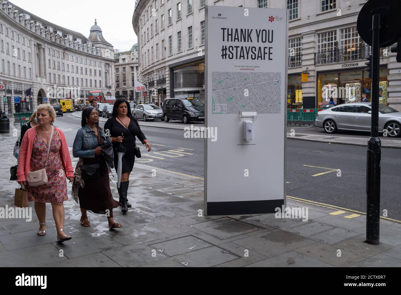 Three woman walk past a hand sanitiser post on Regent Street, during the Coronavirus pandemic, on 24th September, in London, England. New restrictions are being re-introduced by the government after a sudden climb in the Covid infection rate, a predicted 'second spike'. Stock Photo