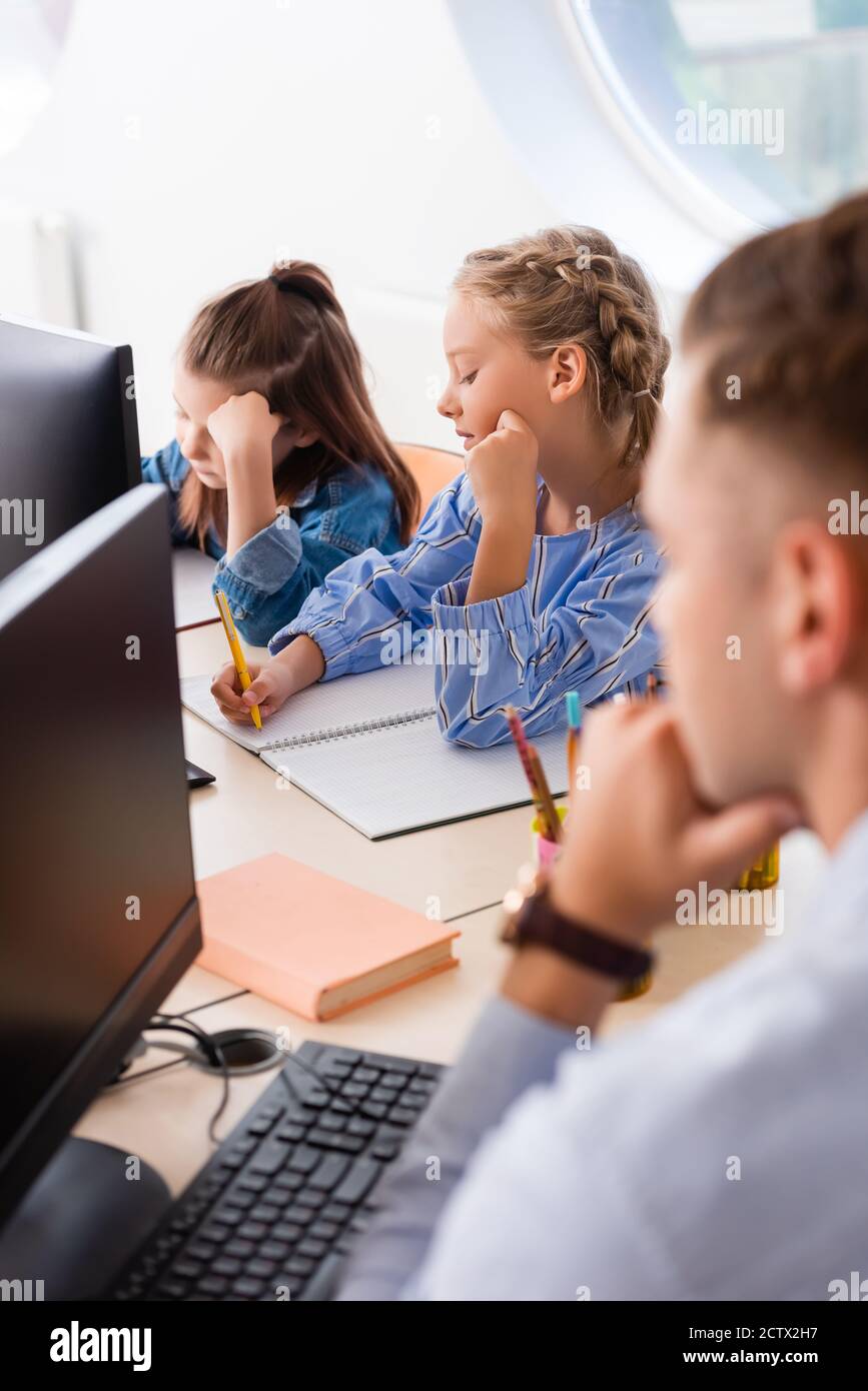 Selective focus of schoolgirls writing on notebook near teacher and ...