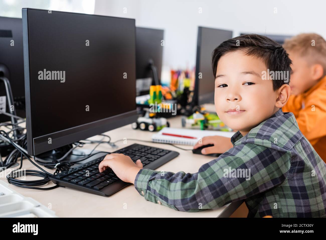 Selective focus of asian schoolboy looking at camera while using computer in classroom Stock Photo