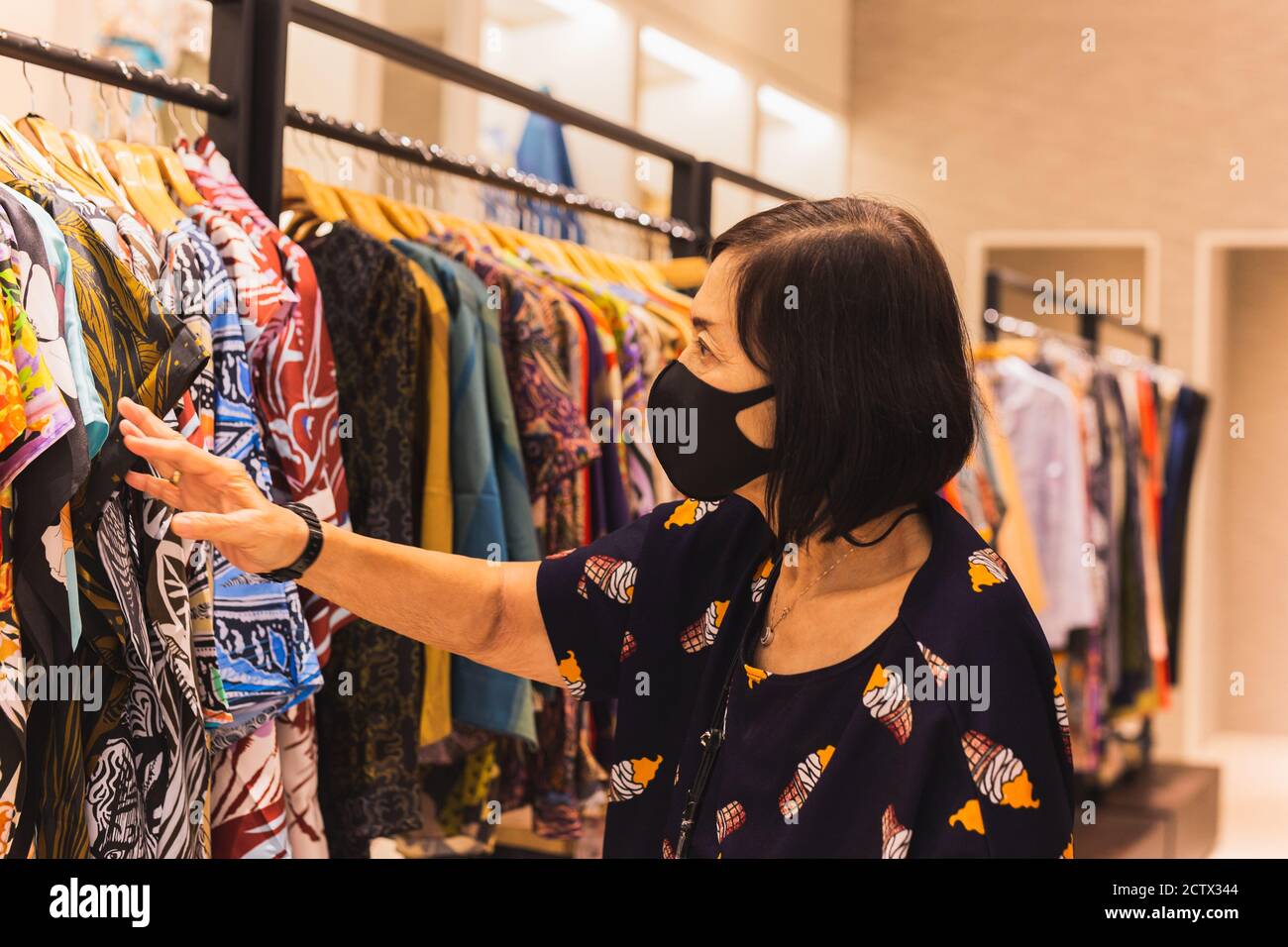 Senior woman with face mask shopping clothes in the department store. Stock Photo