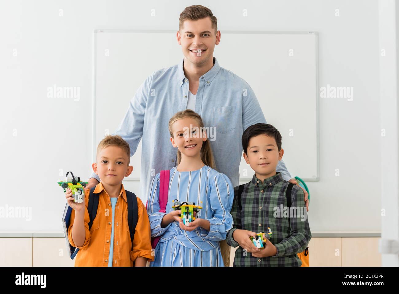 Teacher hugging multicultural pupils with robots in stem school Stock Photo