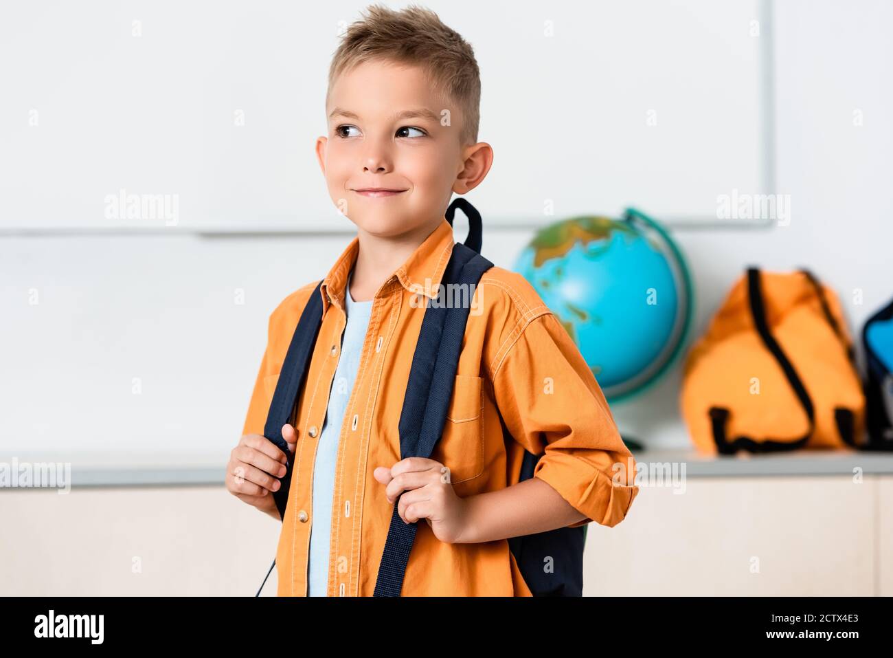 Schoolboy holding backpack while looking away in classroom Stock Photo