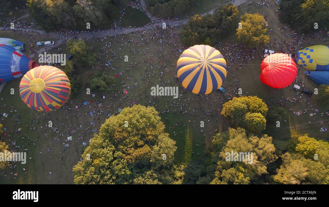 Aerial view of people looking at how hot air balloons prepare for an summer evening flying in park in small european city, Kiev region, Ukraine Stock Photo