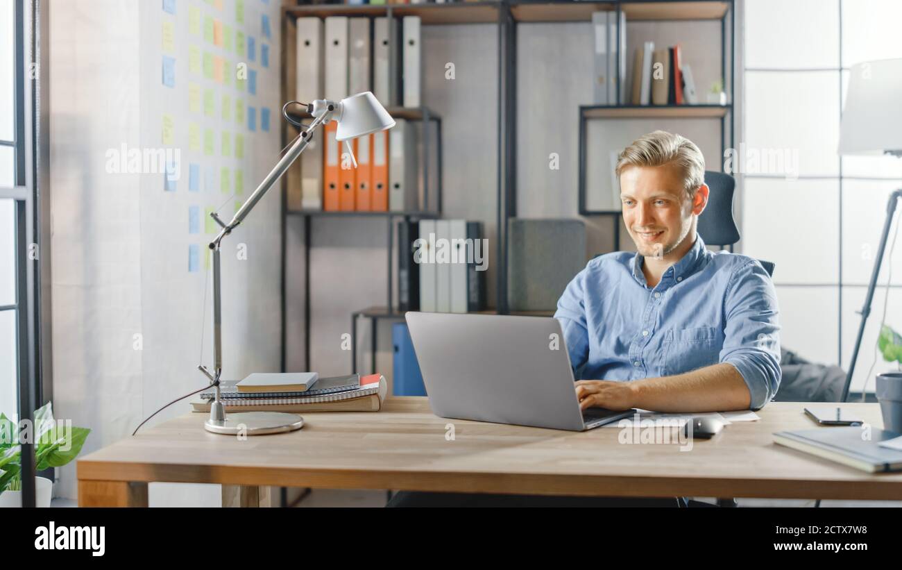 Creative Entrepreneur Sitting at His Desk Works on a Laptop in the Stylish Office, Uses Software for Social Media Apps, Emailing Business Associates Stock Photo