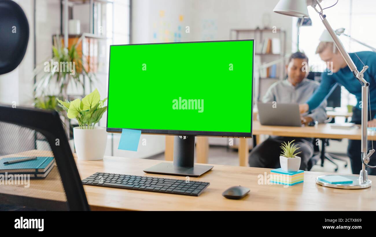 Mock-up Screen Desktop Computer Standing on the Desk in the Modern Creative Office. In the Background Bright Studio where Diverse Team of Young Stock Photo