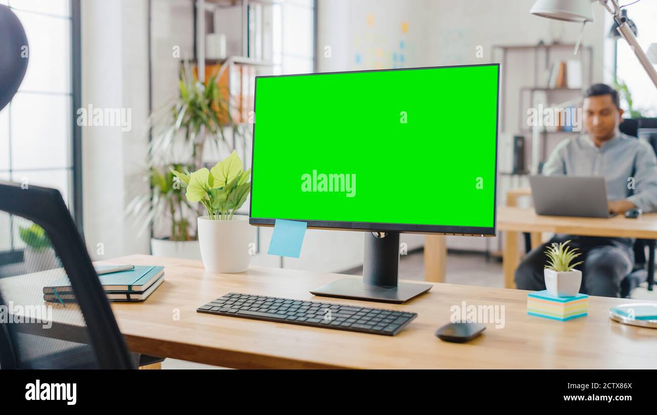 Mock-up Screen Desktop Computer Standing on the Desk in the Modern Creative Office. In the Background Bright Studio Apartment where Diverse Team of Stock Photo