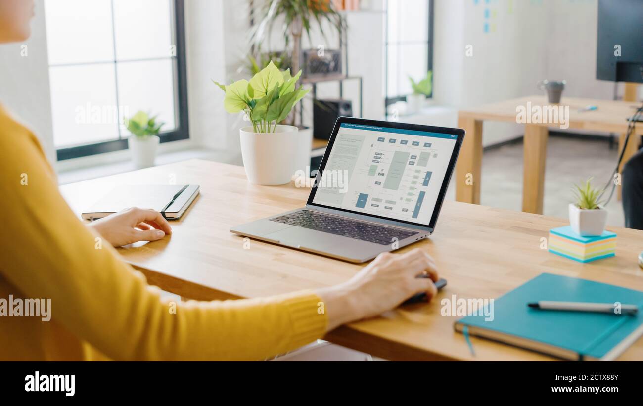 Over the Shoulder: Female Engineer Developer Sitting at Her Desk Using Laptop with Hardware Microchip Design. Office where Diverse Team of Young Stock Photo