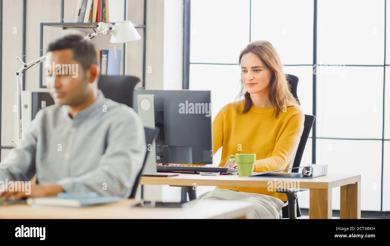 Handsome Indian Information Technology and Brilliant Female Data Specialist Sitting at Their Desks work on Desktop Computers. Modern Office with Stock Photo