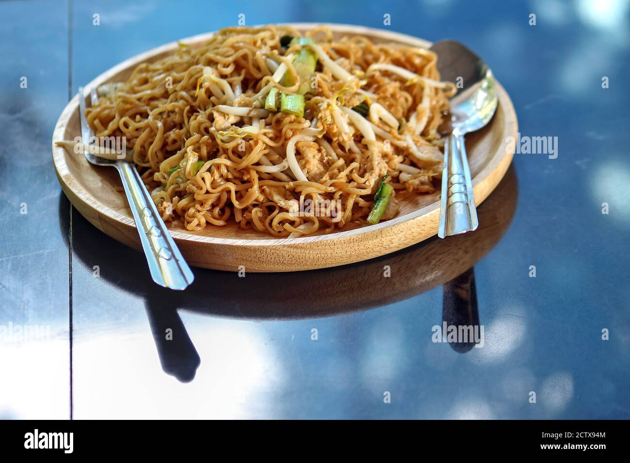Stir-fry instant noodles, fast food, easy to make at home, put them in a round wooden dish, placed on the marble table in the kitchen. Stock Photo
