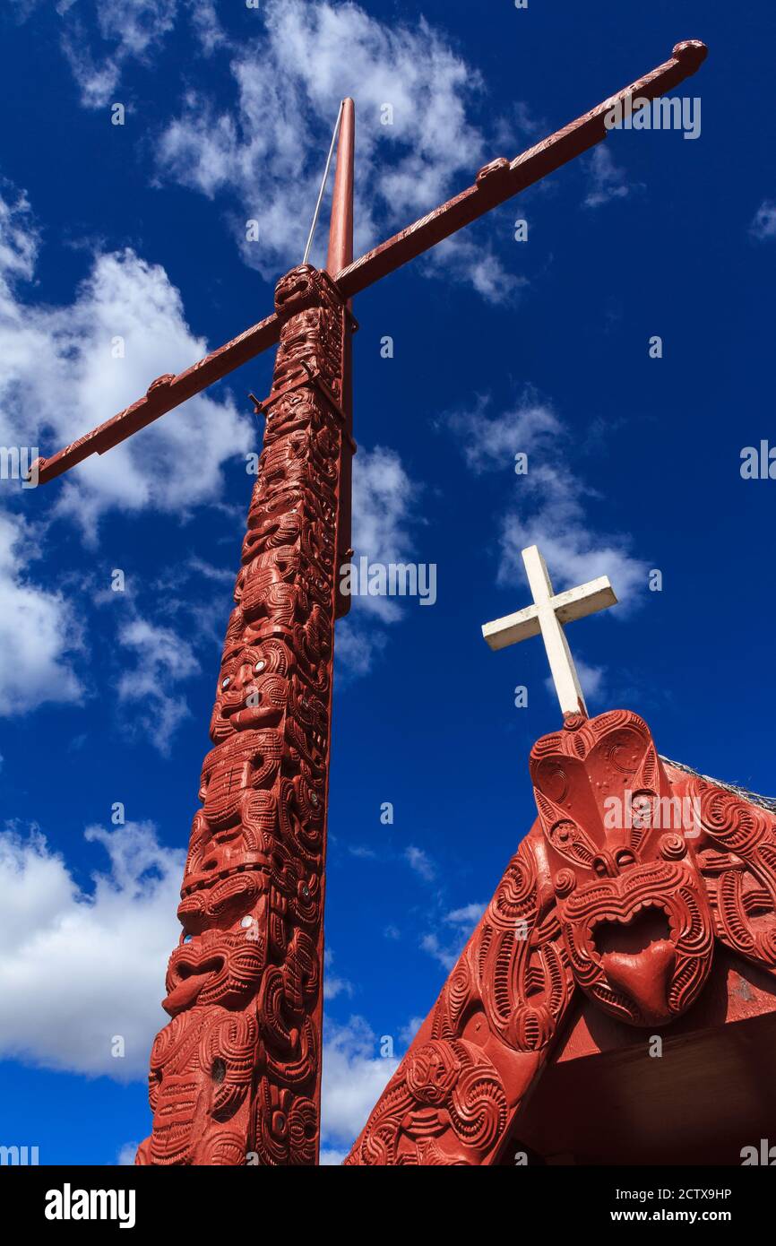 New Zealand Maori carving. A flagstaff and part of a meeting house, displaying a mix of traditional and Christian elements. Rotorua, New Zealand Stock Photo