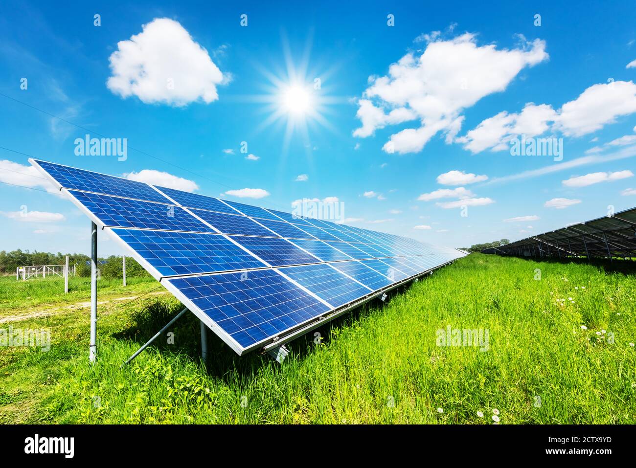 Solar panel under blue sky with sun. Green grass and cloudy sky. Alternative energy concept Stock Photo