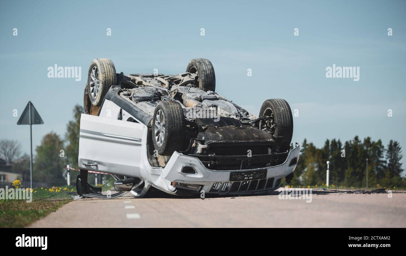 Horrific Traffic Accident, Rollover Smoking and Burning Vehicle Lying on its Roof in the Middle of the Road after Collision. Daytime Crash Scene with Stock Photo
