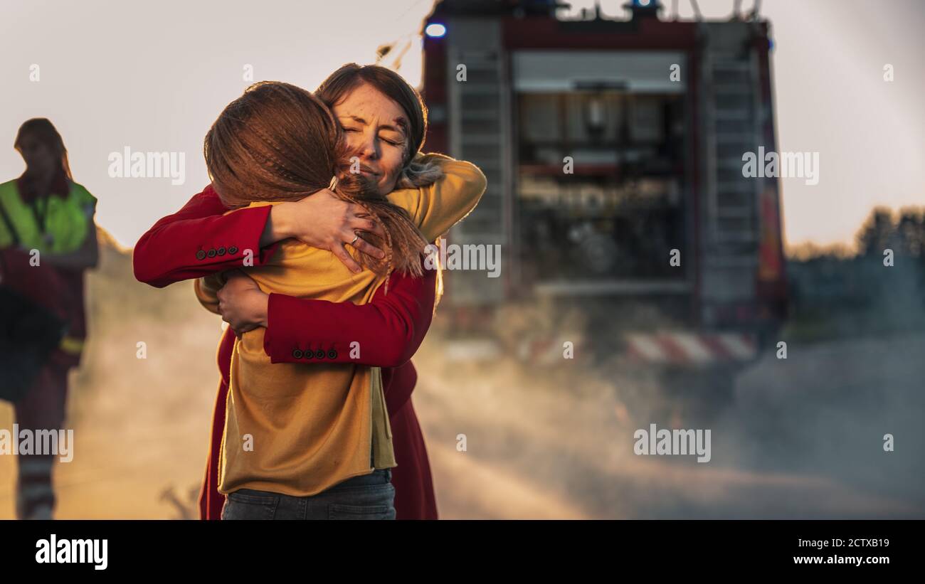 Car Crash Traffic Accident: Injured Young Girl Reunites with Her Loving Mother. In the Background Fire engine and Courageous Paramedics and Firemen Stock Photo