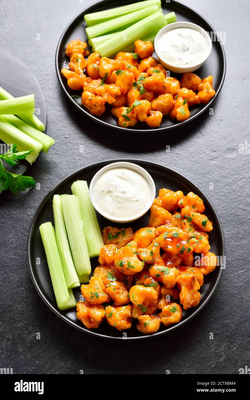 Cauliflower buffalo wings with celery and sauce on plate over black
