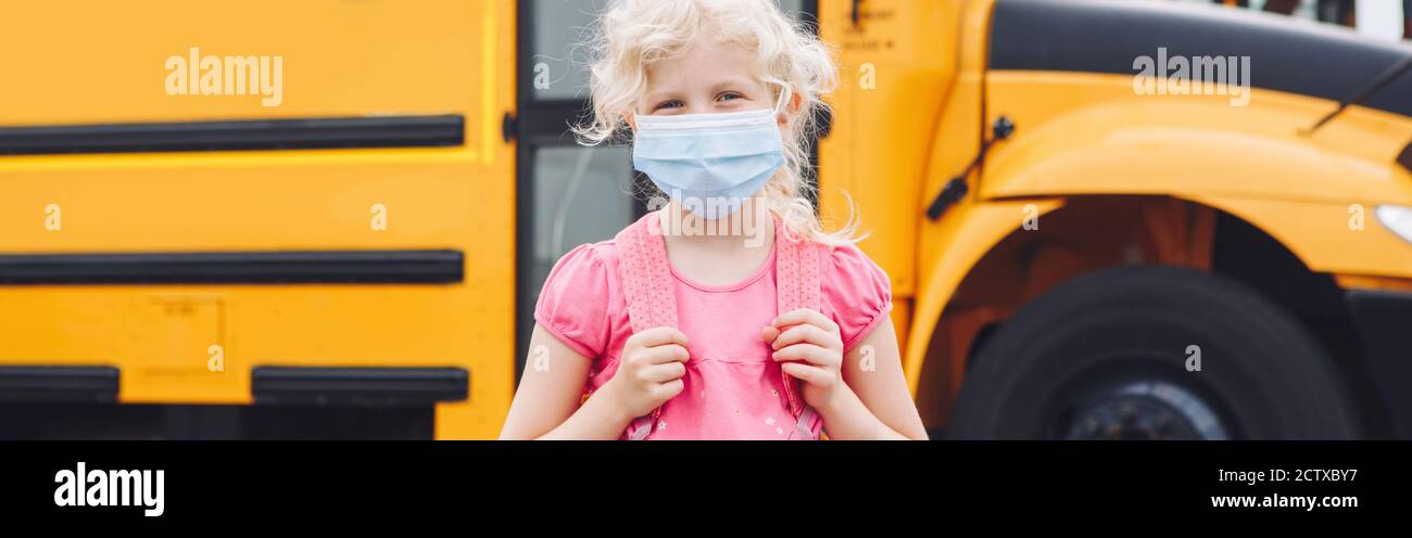 Girl student in face mask near yellow bus. Kid with personal protective equipment on face. Education and back to school in September. New normal Stock Photo